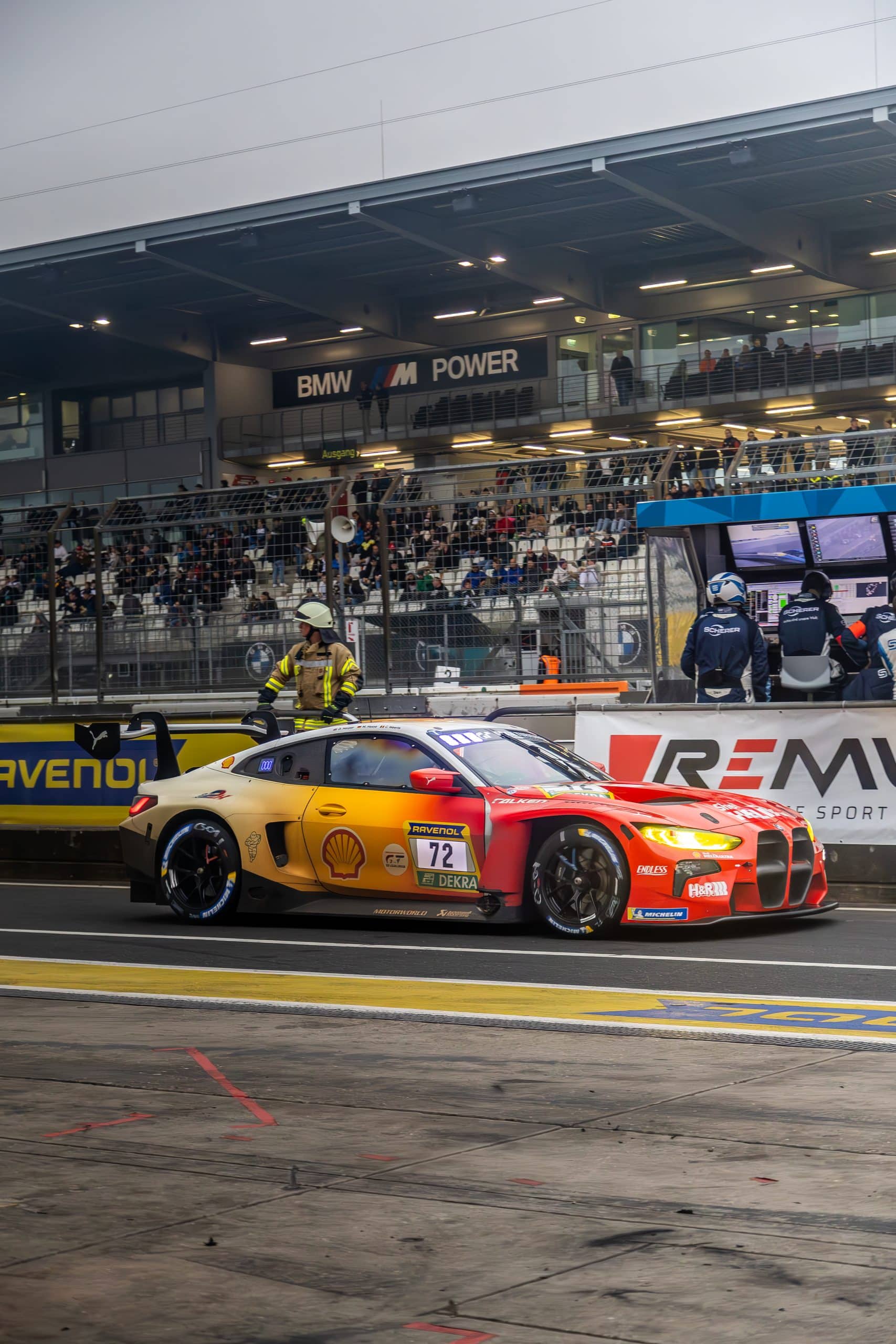 A race car passing at speed with warm light and grandstand atmosphere.