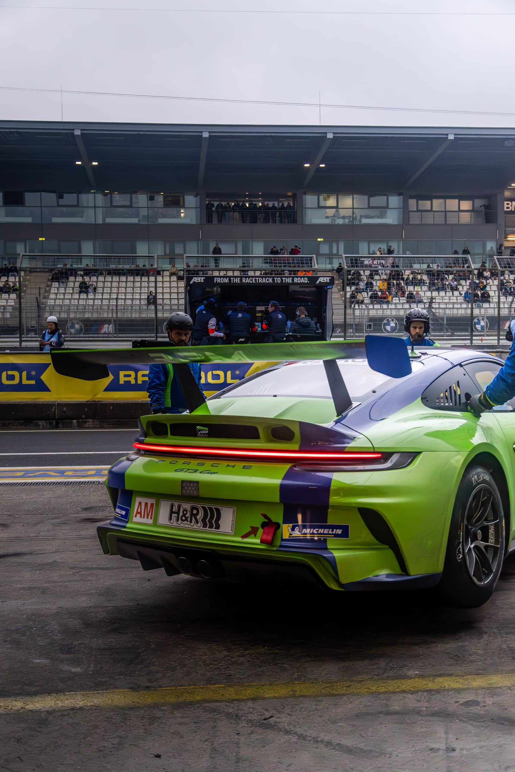 A green racing car photographed from the rear in the paddock.