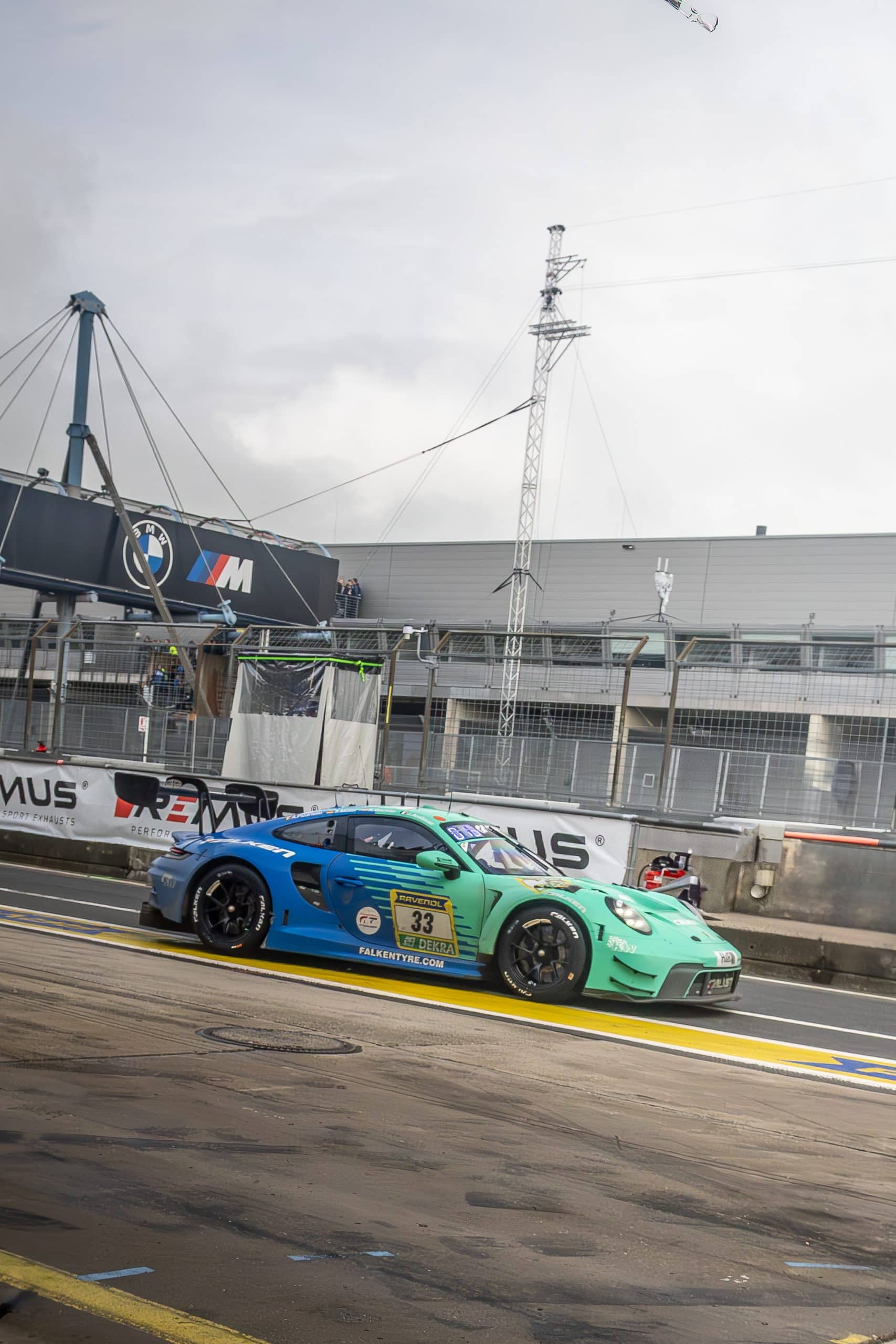 A green race car exiting a circuit corner in wet conditions.