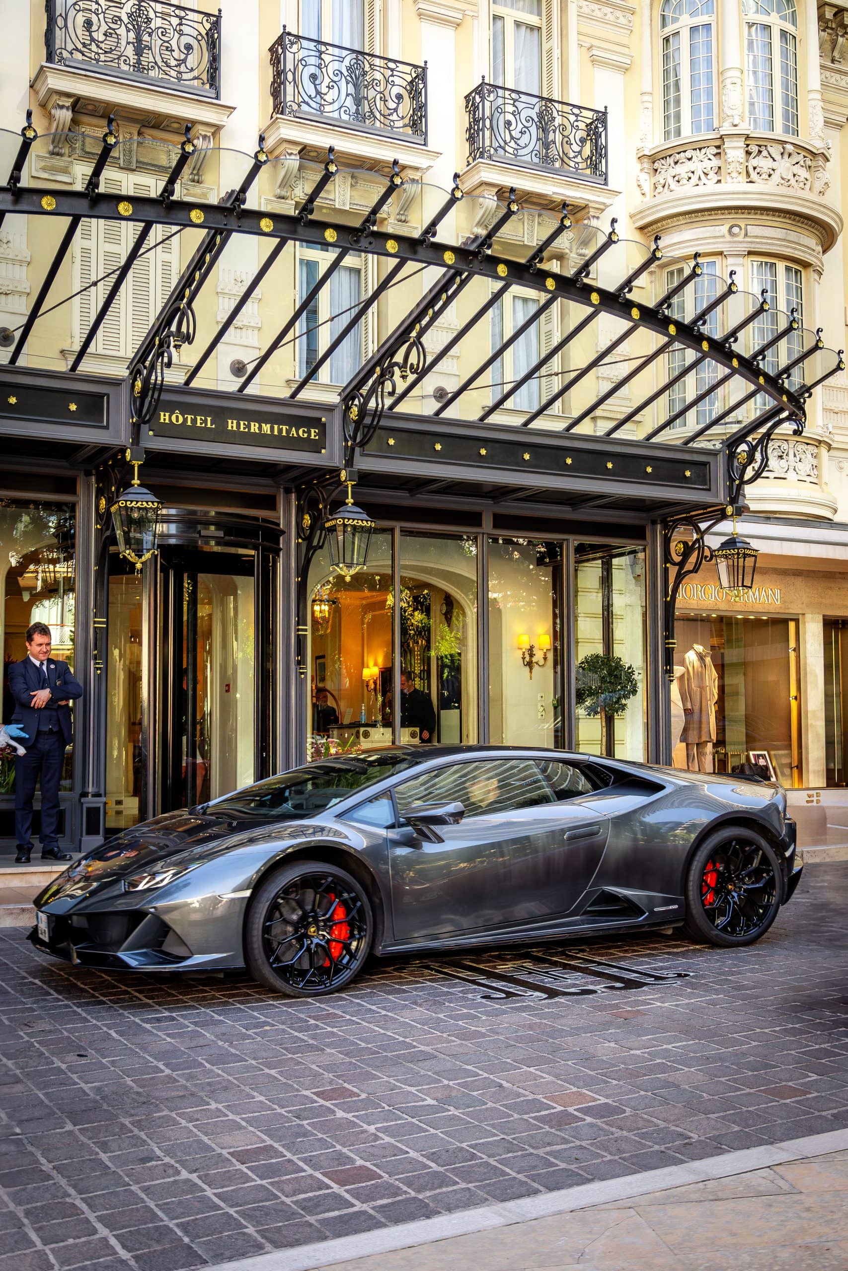 A grey supercar framed in front of the Hotel Hermitage entrance.