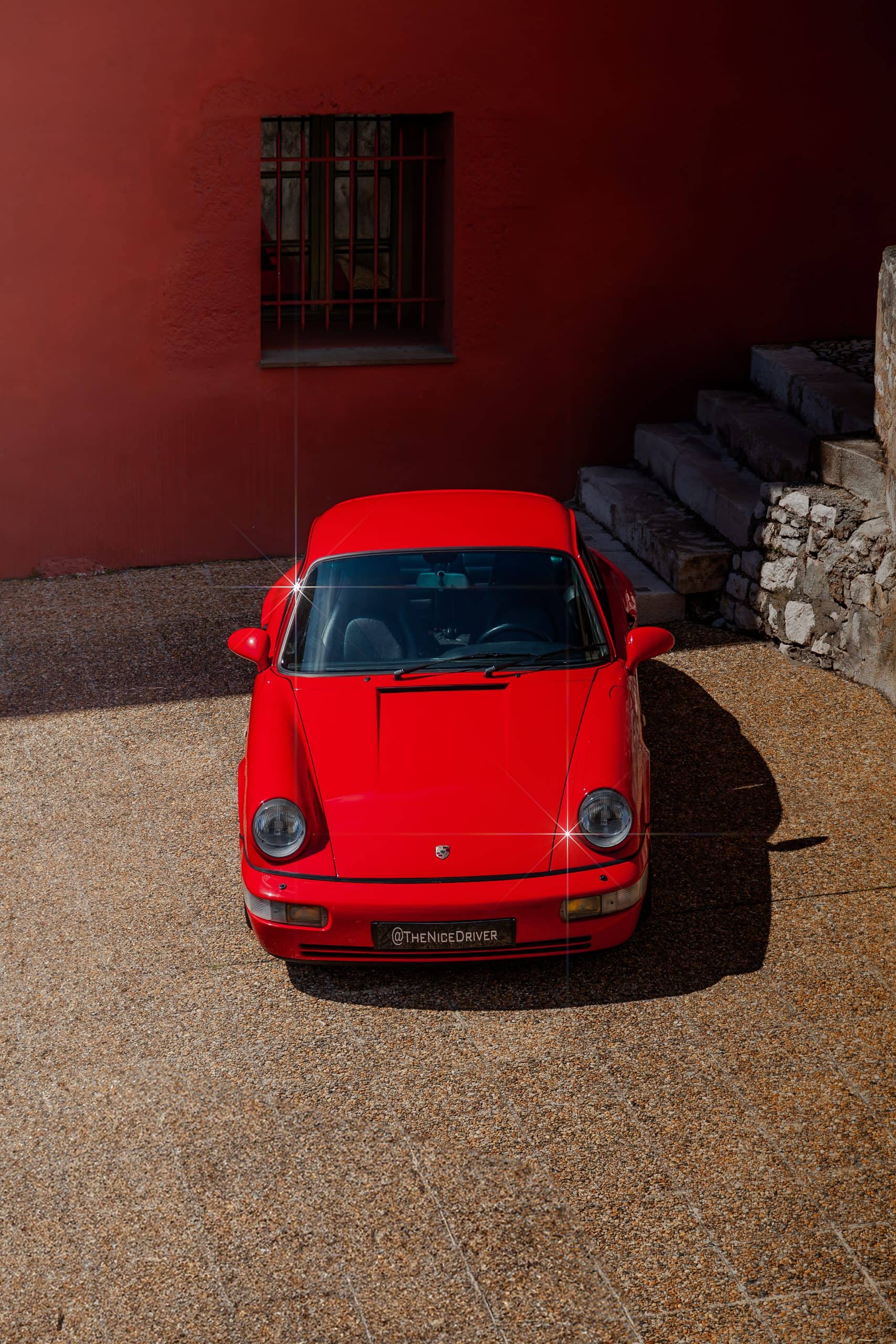 A red coupe photographed head-on inside a shadowed courtyard.