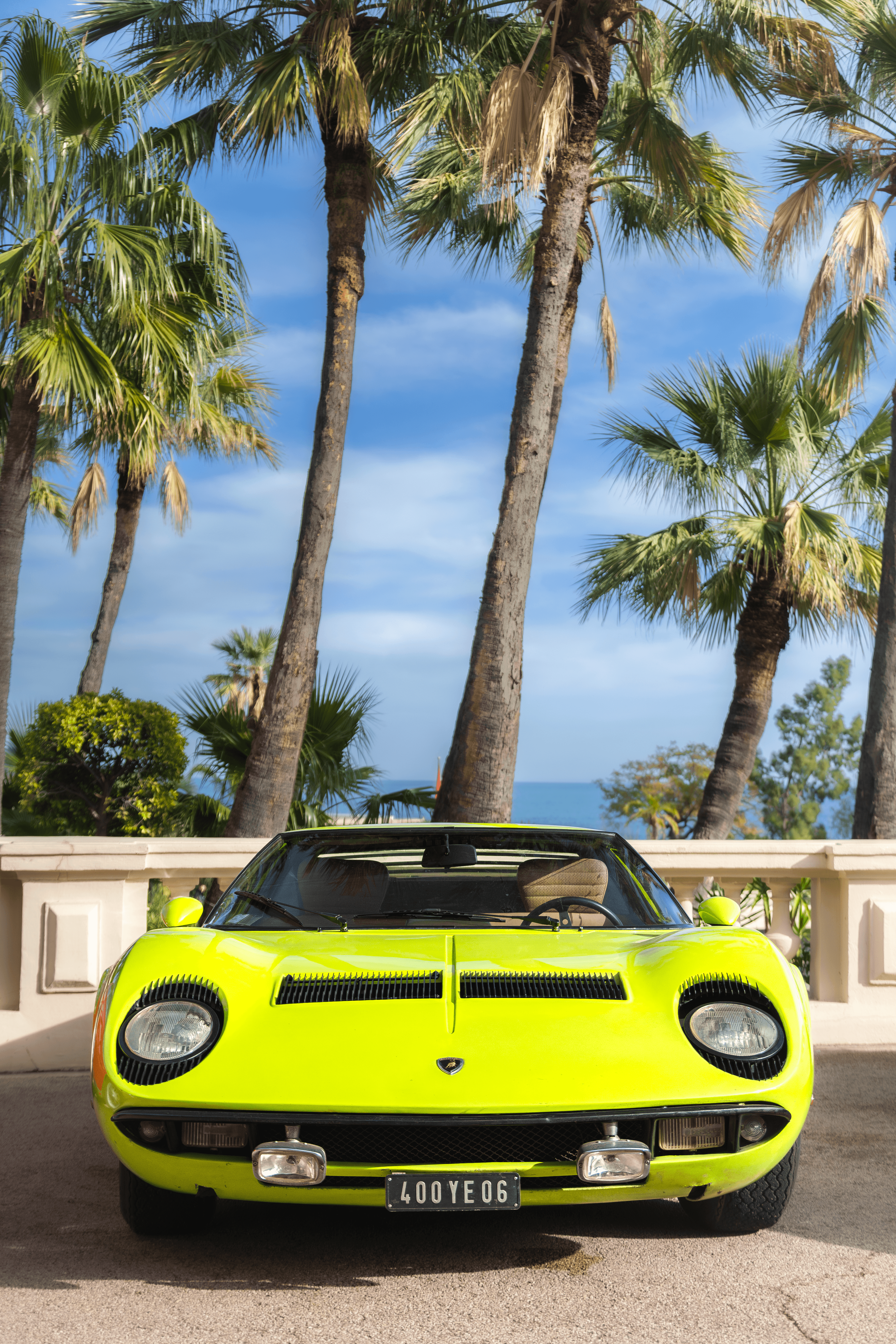 An acid green coupe photographed under palm trees with a bright editorial palette.