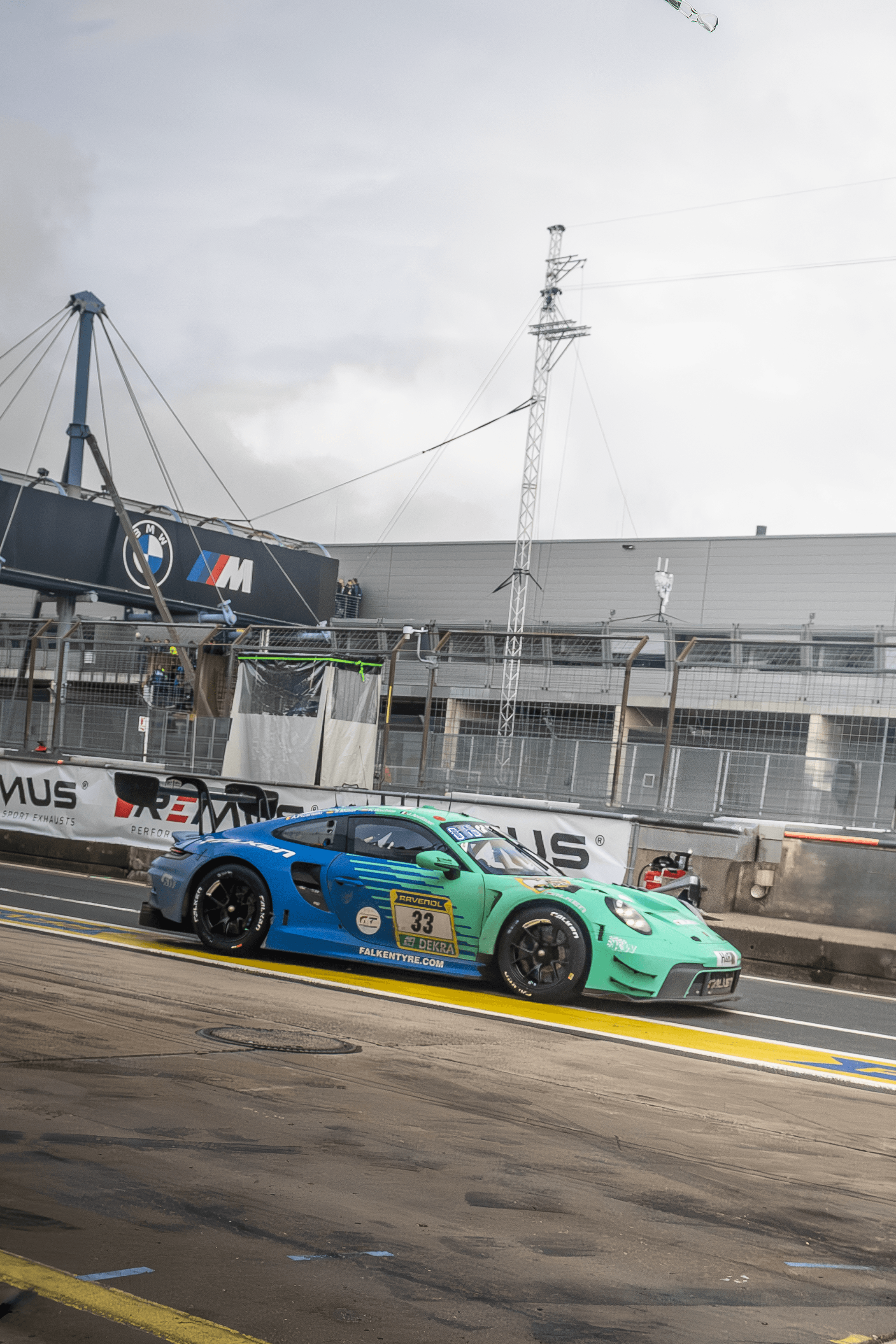 A green race car exiting a circuit corner in wet conditions.