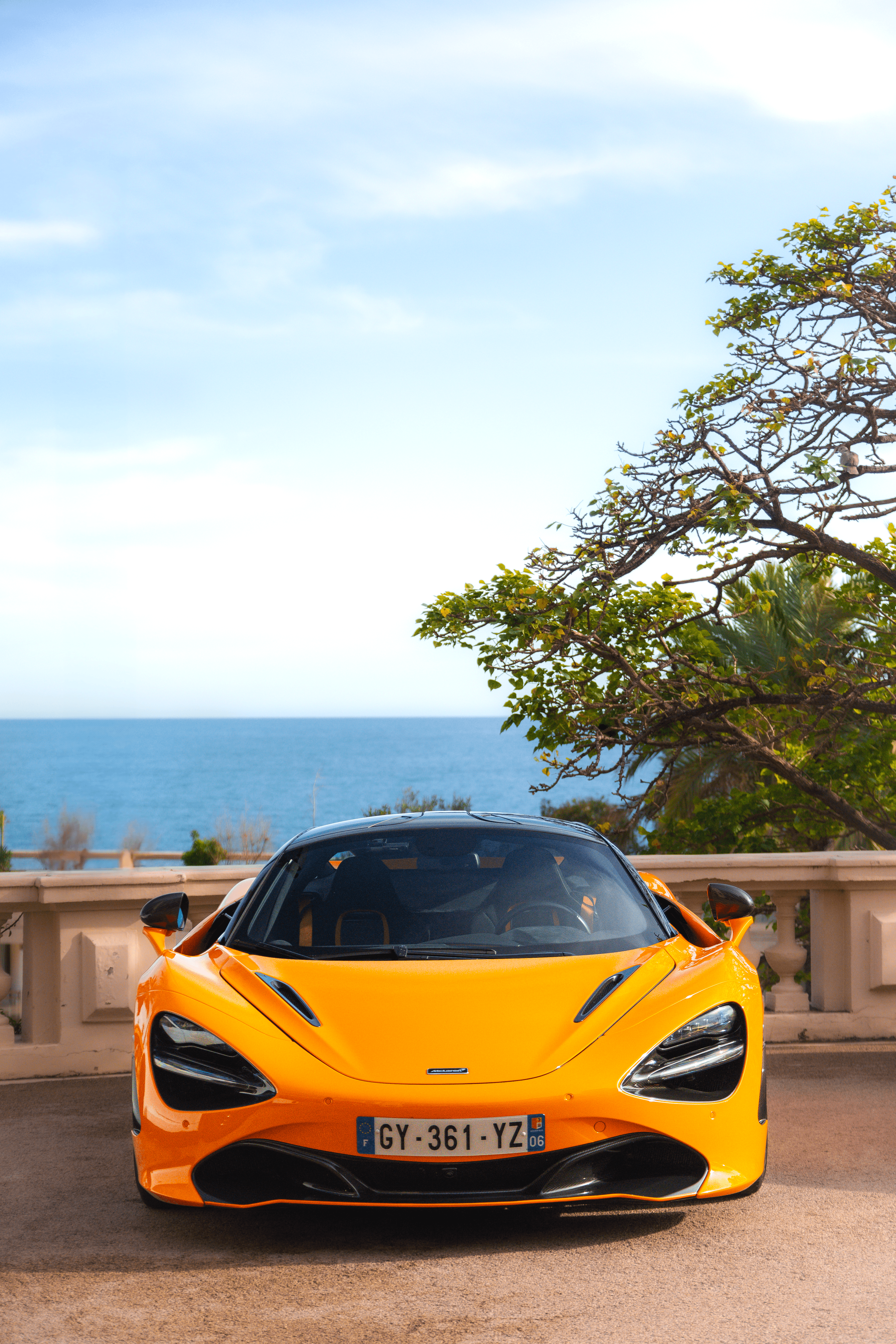 An orange supercar photographed front-on with sea and sky behind it.