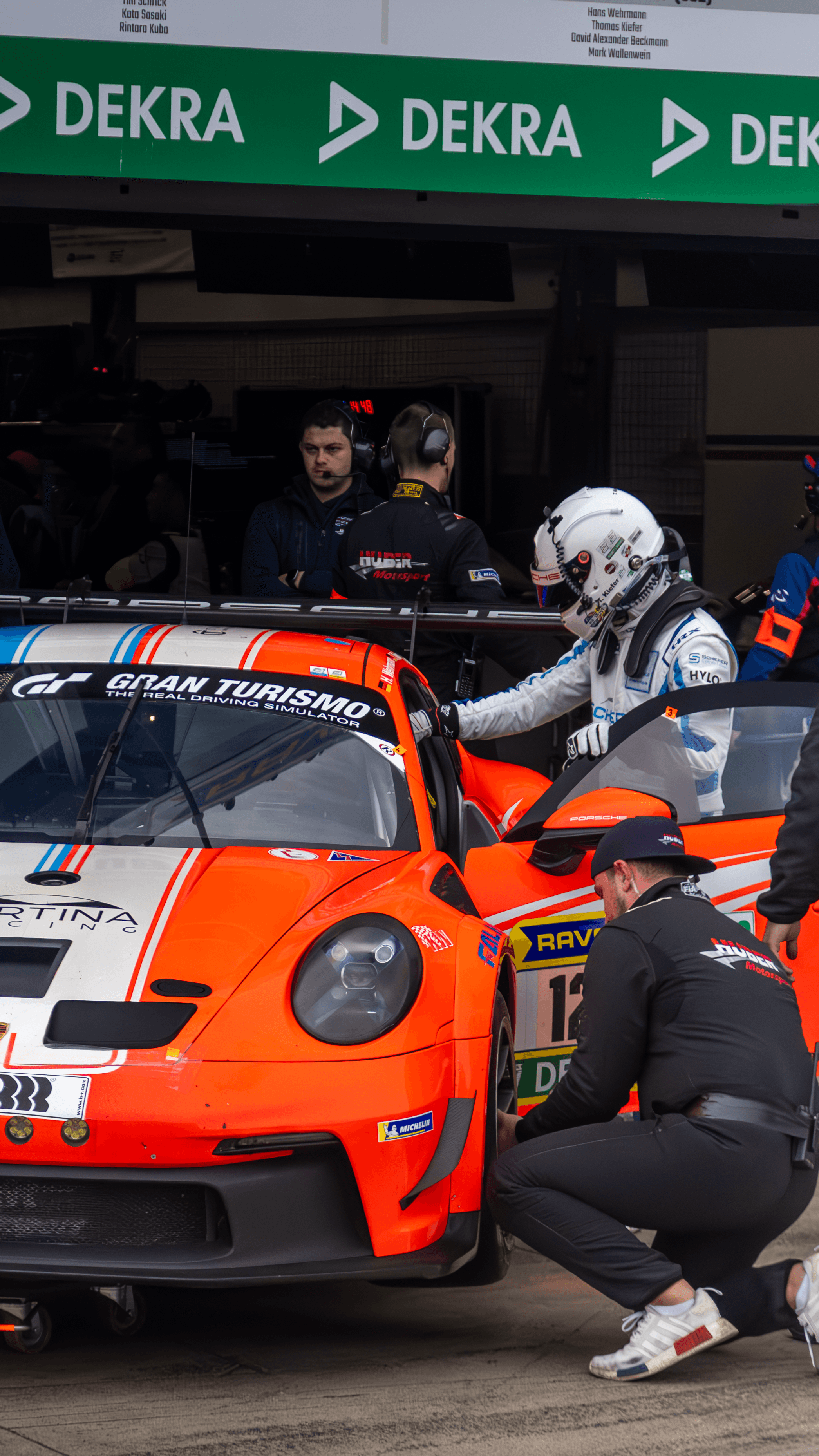 An orange GT race car photographed in the paddock with crew nearby.