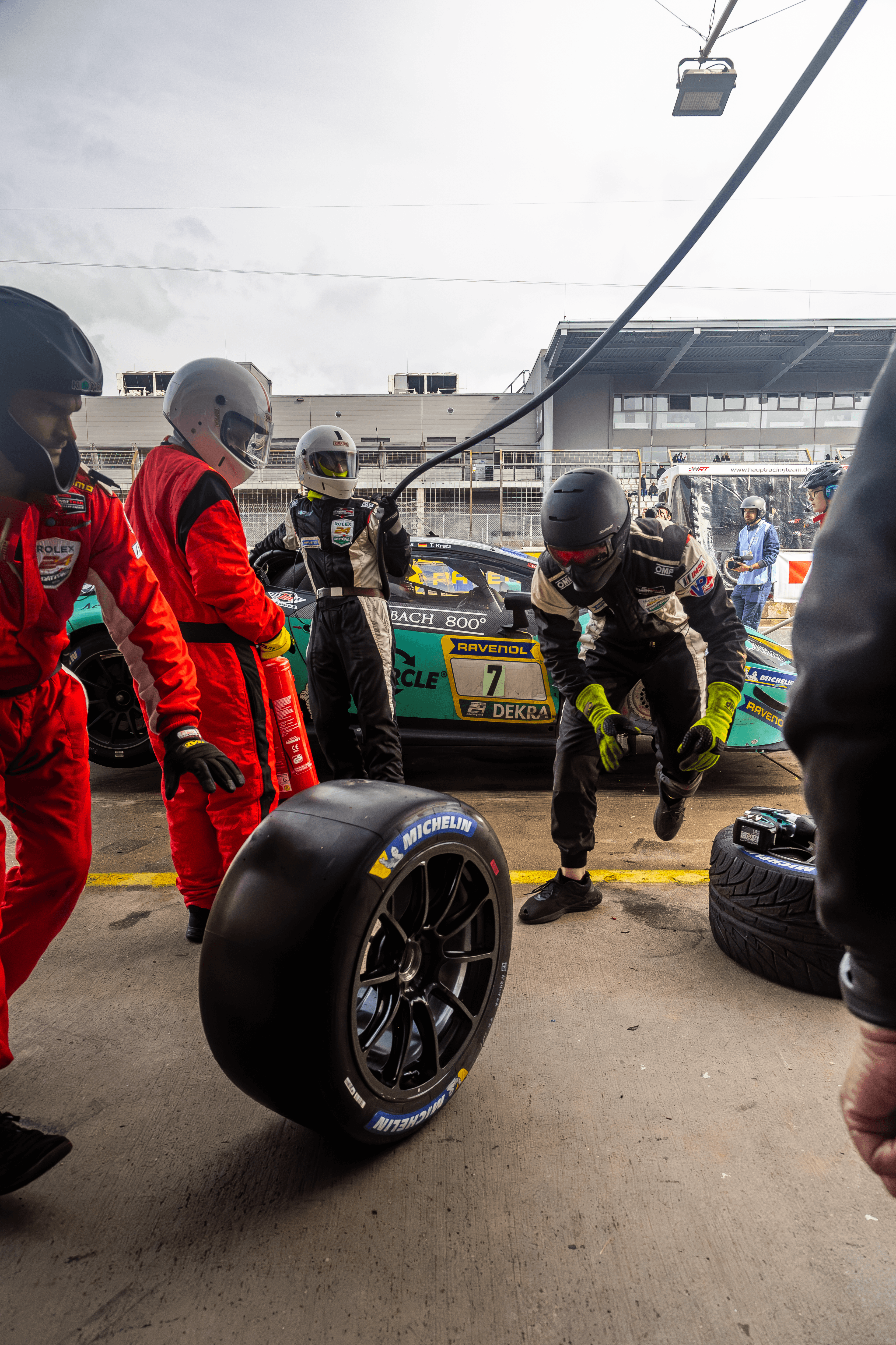 A pit lane detail study with a racing wheel and crew members.