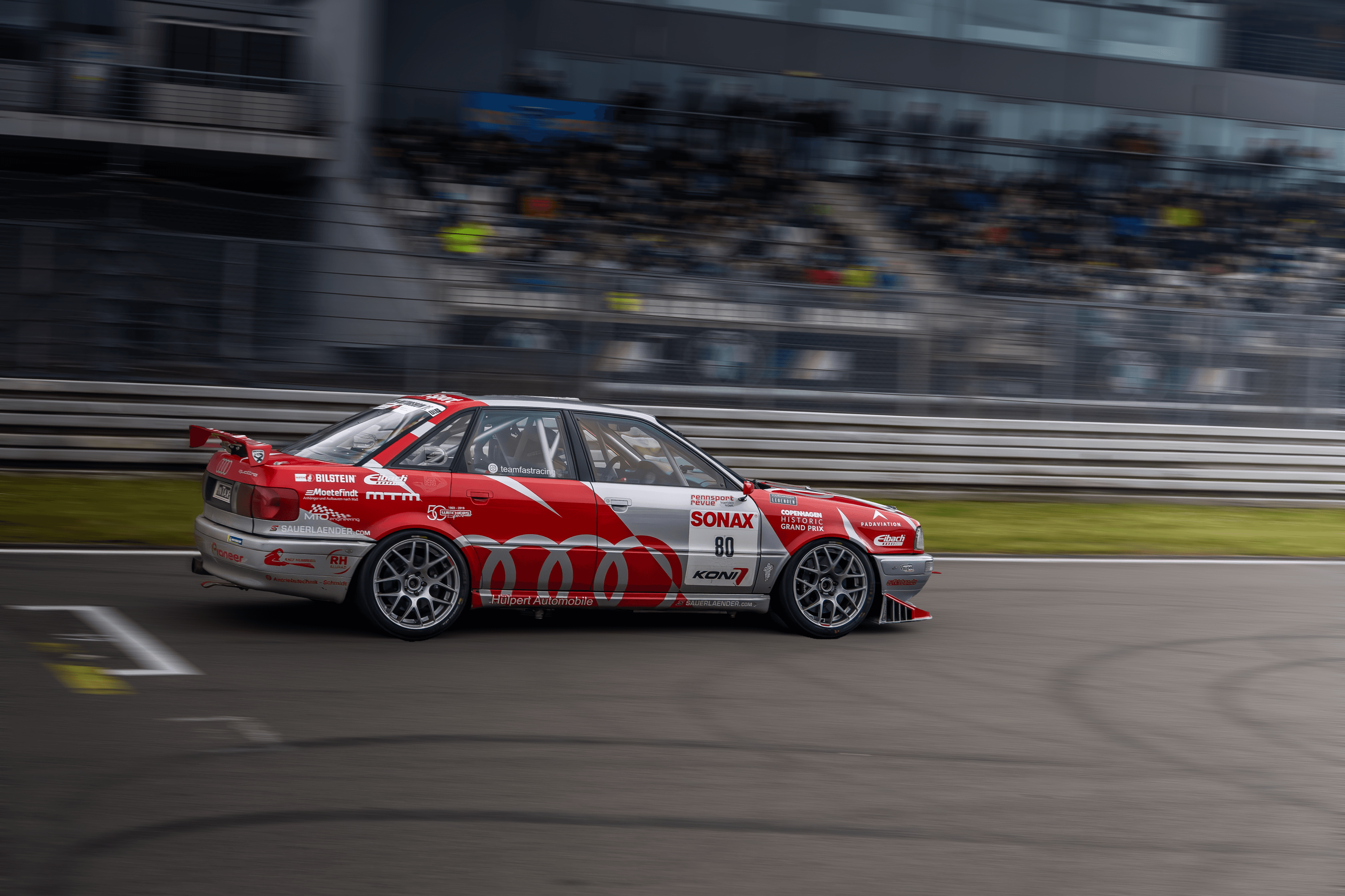 A red liveried race car captured in motion during a circuit session.