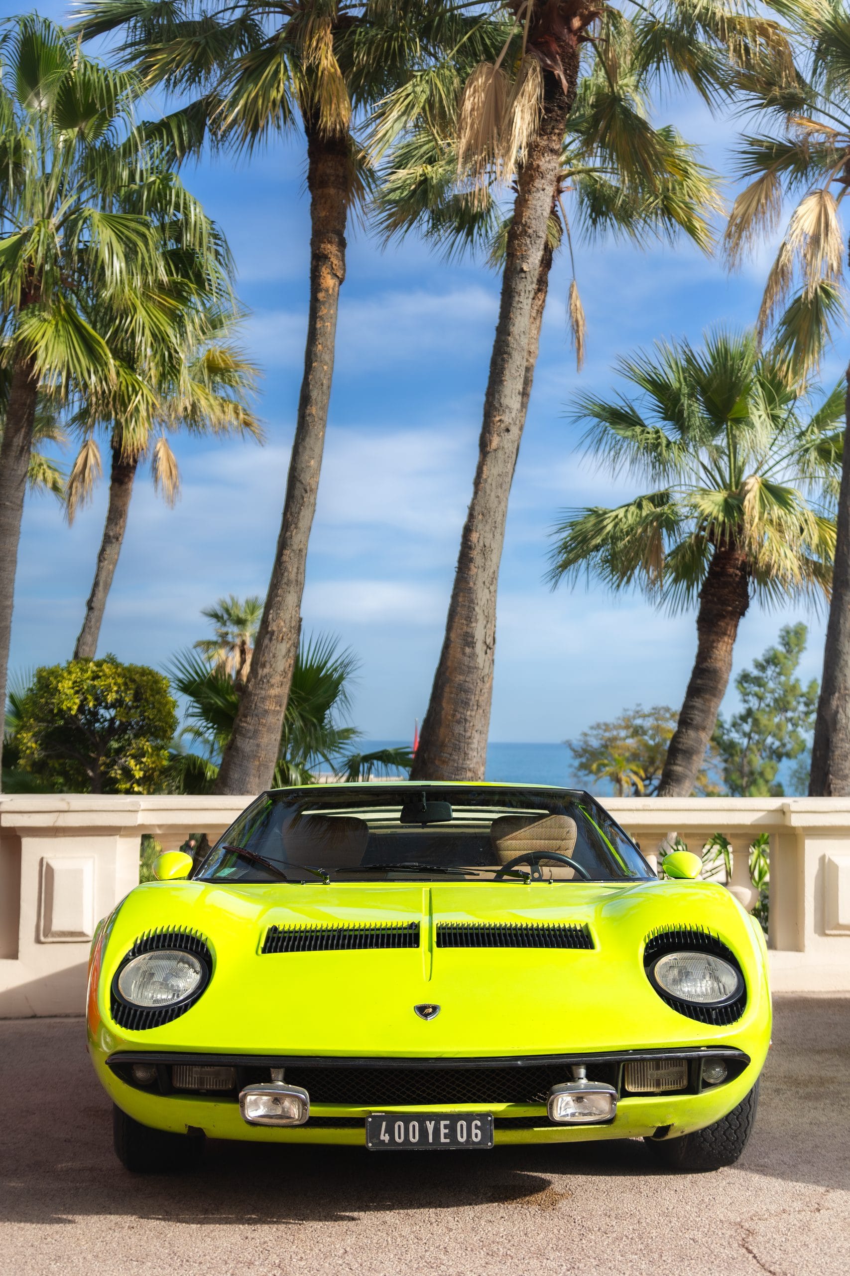 Acid green sports car facing the camera on a seafront promenade lined with palms.