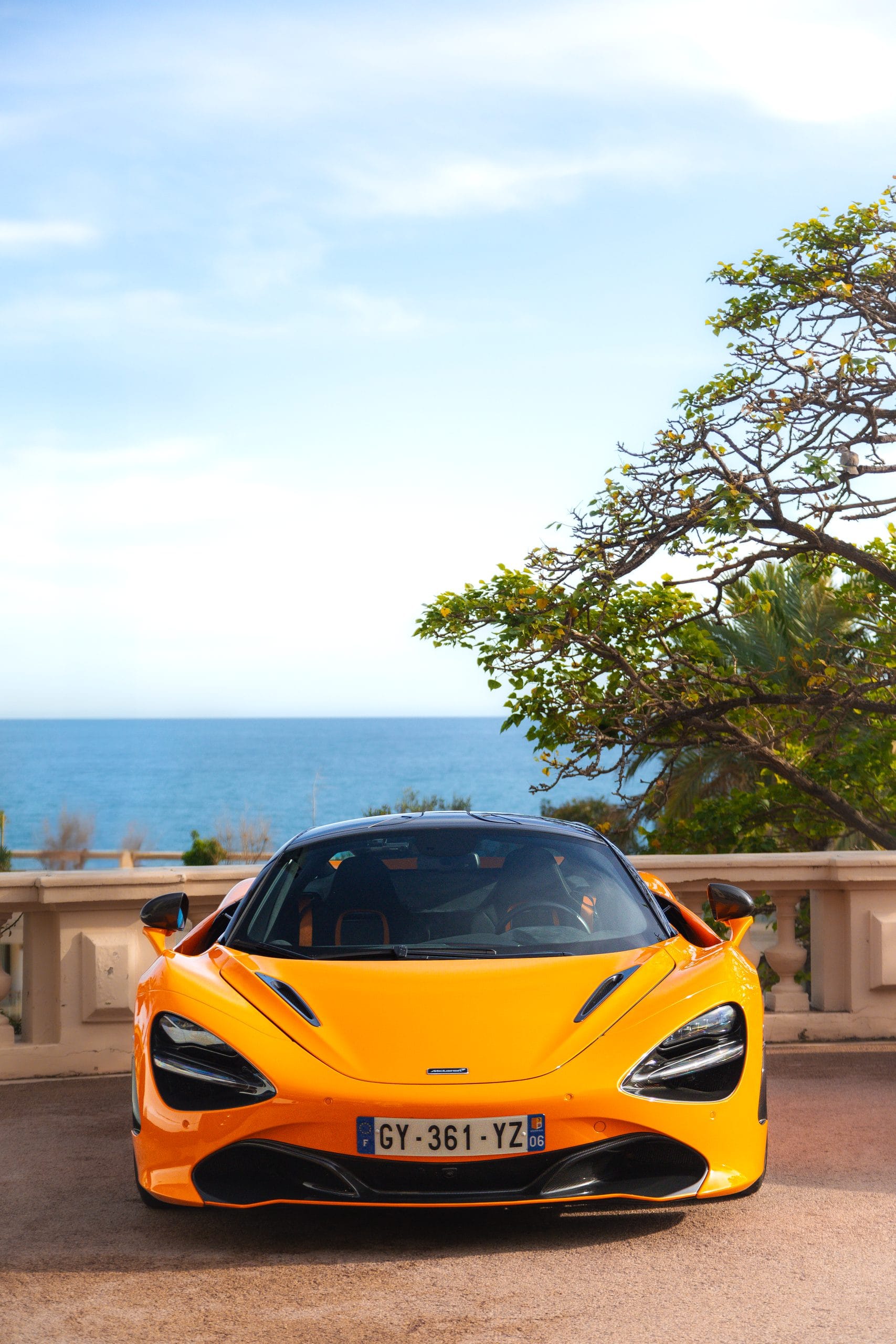 Orange supercar on a terrace, the sea and the horizon behind it.