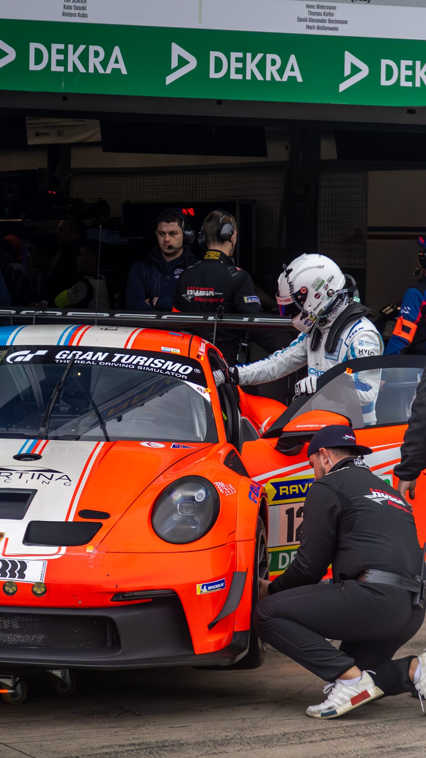 Orange GT car in a pit box, a driver in a white helmet stepping in.