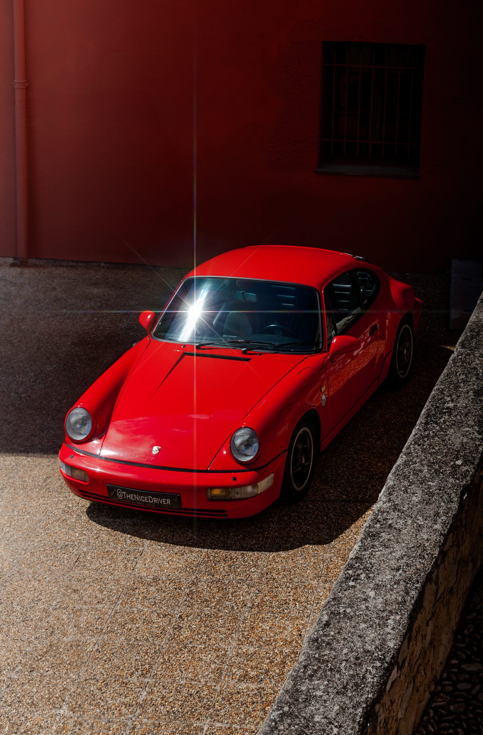 The red 911 parked on gravel, light falling across its bonnet.