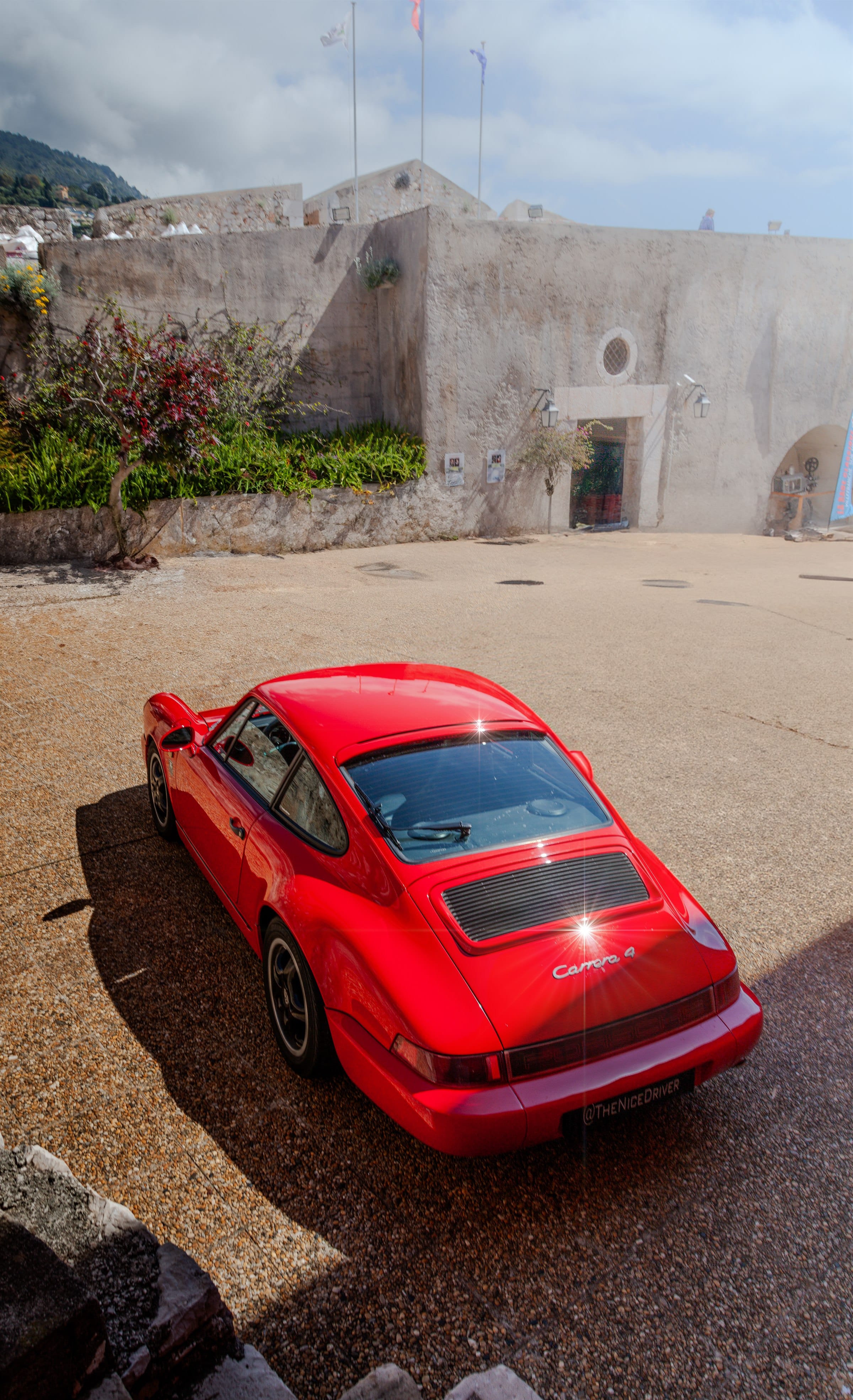 The red 911 approaching along a stone wall, hills behind.