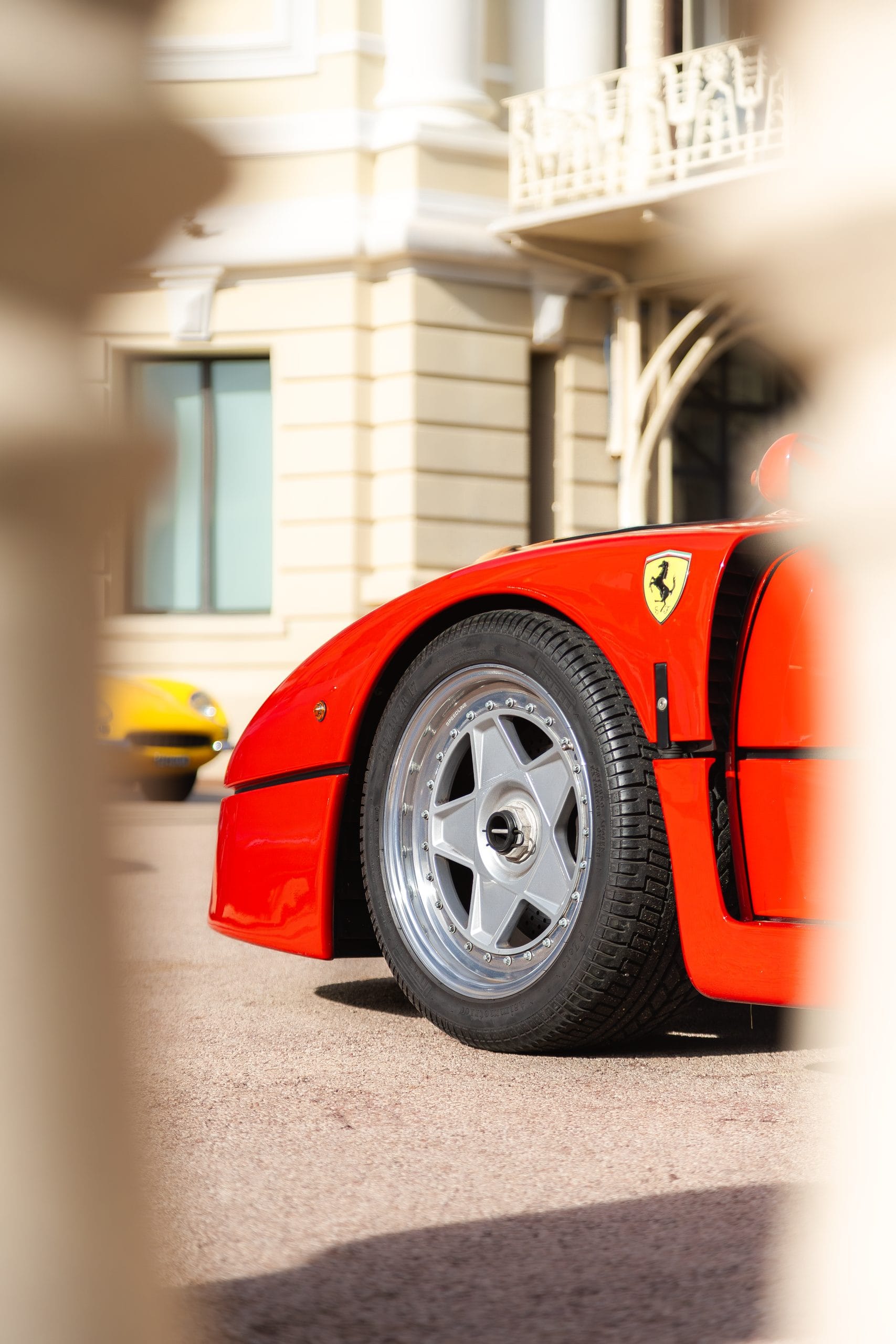 Red supercar's rear wheel arch and silver five spoke wheel, framed by a stone column.