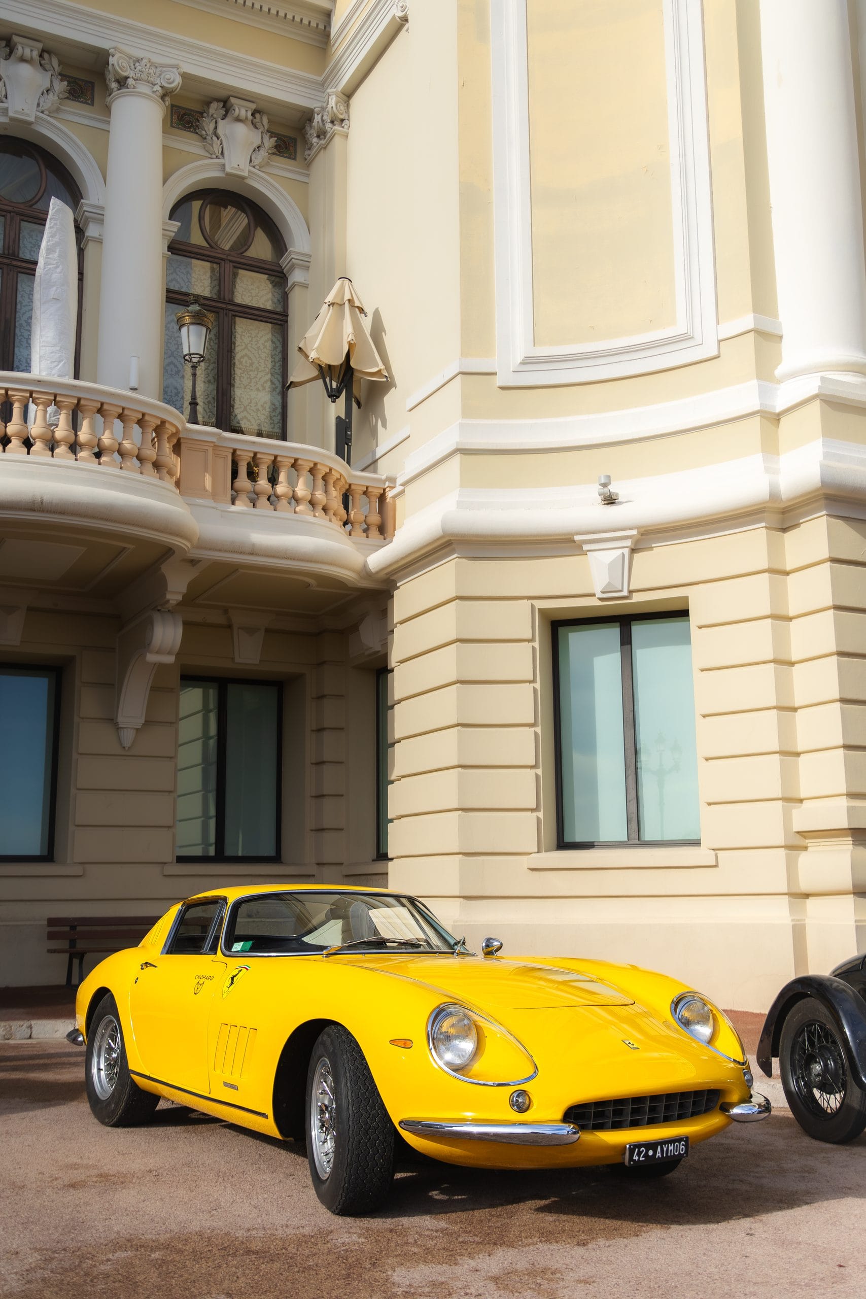 Yellow classic coupe in front of a cream stone facade with balconies.