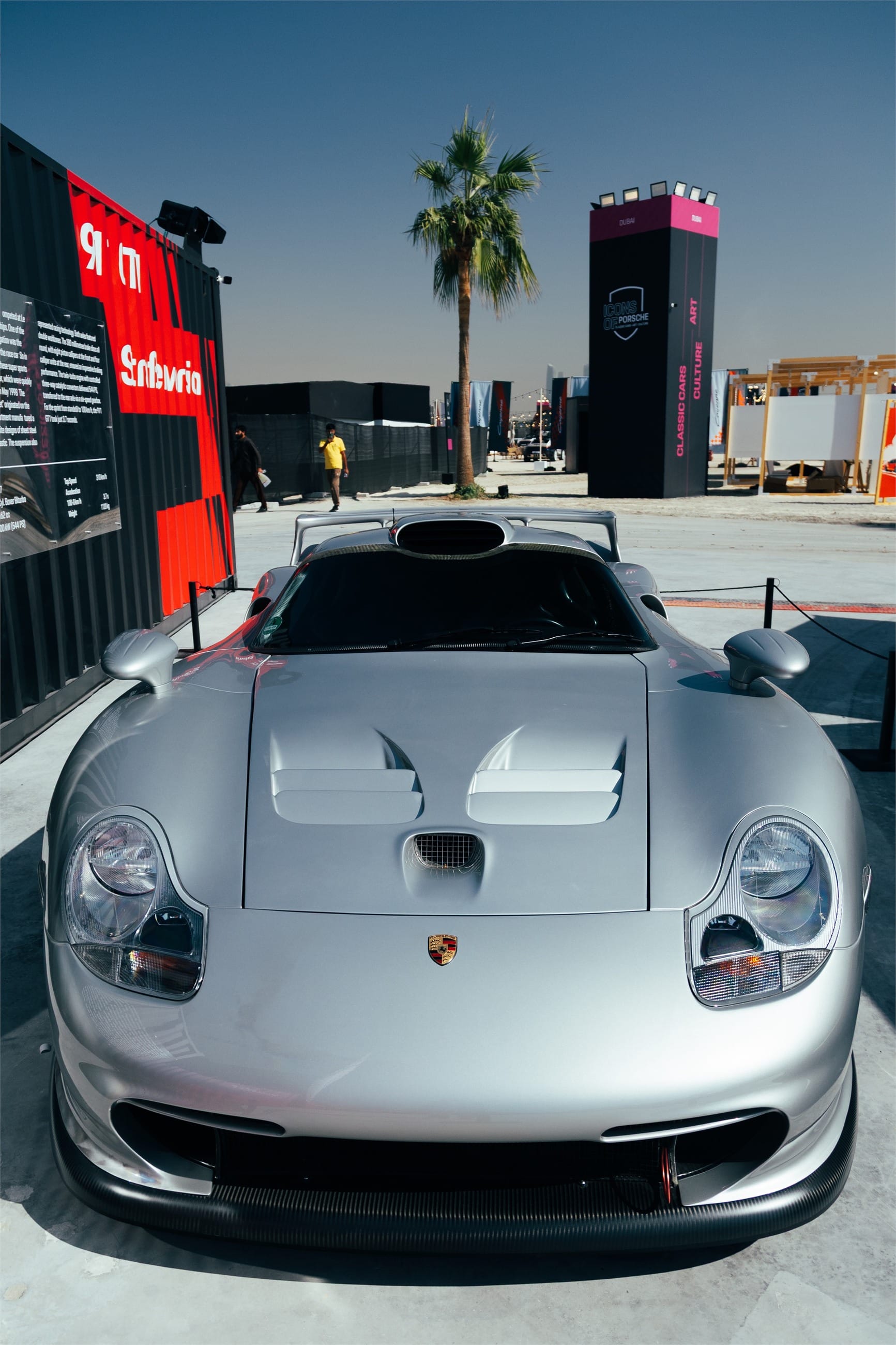 Silver GT racing car seen head on, palm and skyline behind.