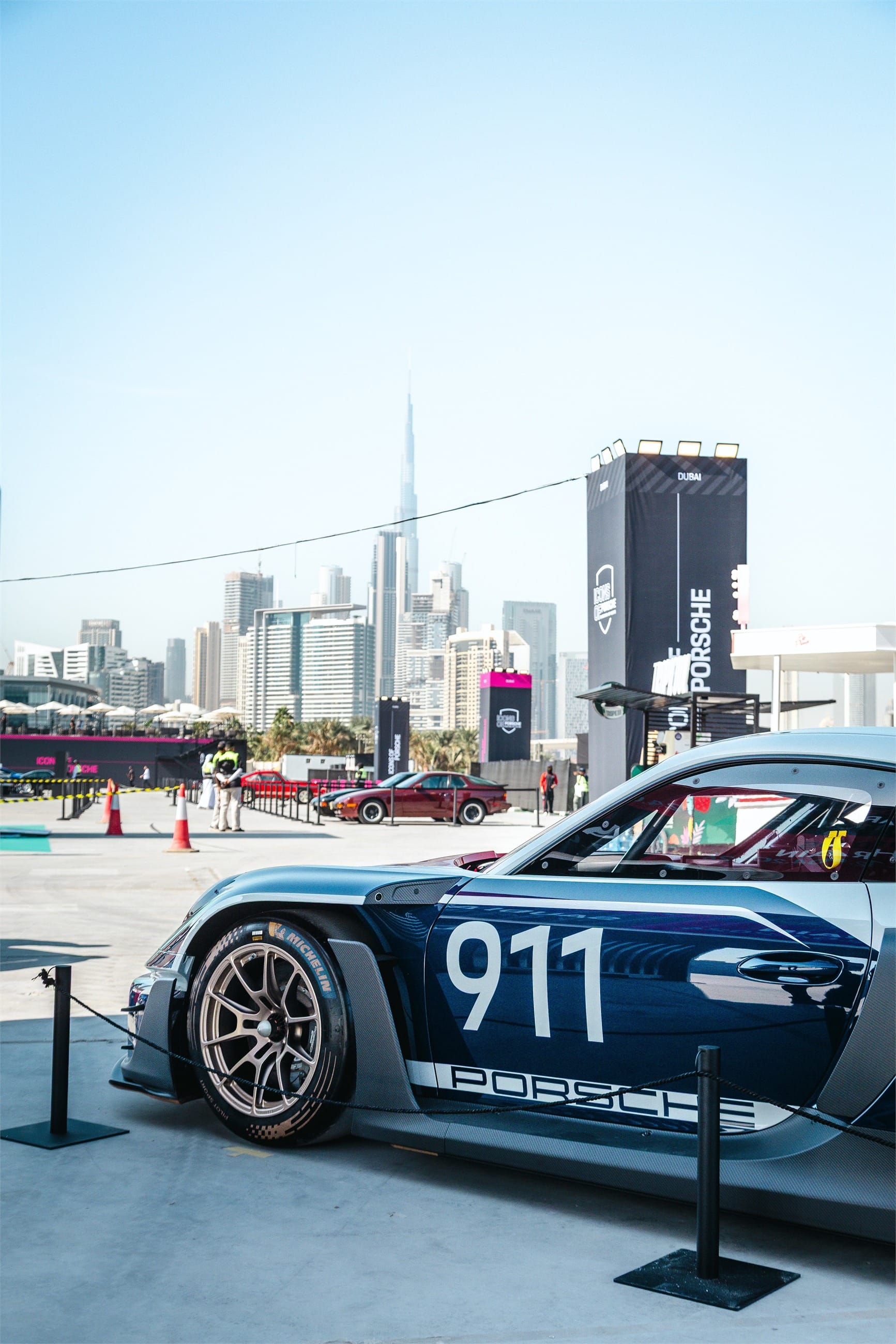 Blue and white racing 911 with a large 911 number, skyline in the distance.