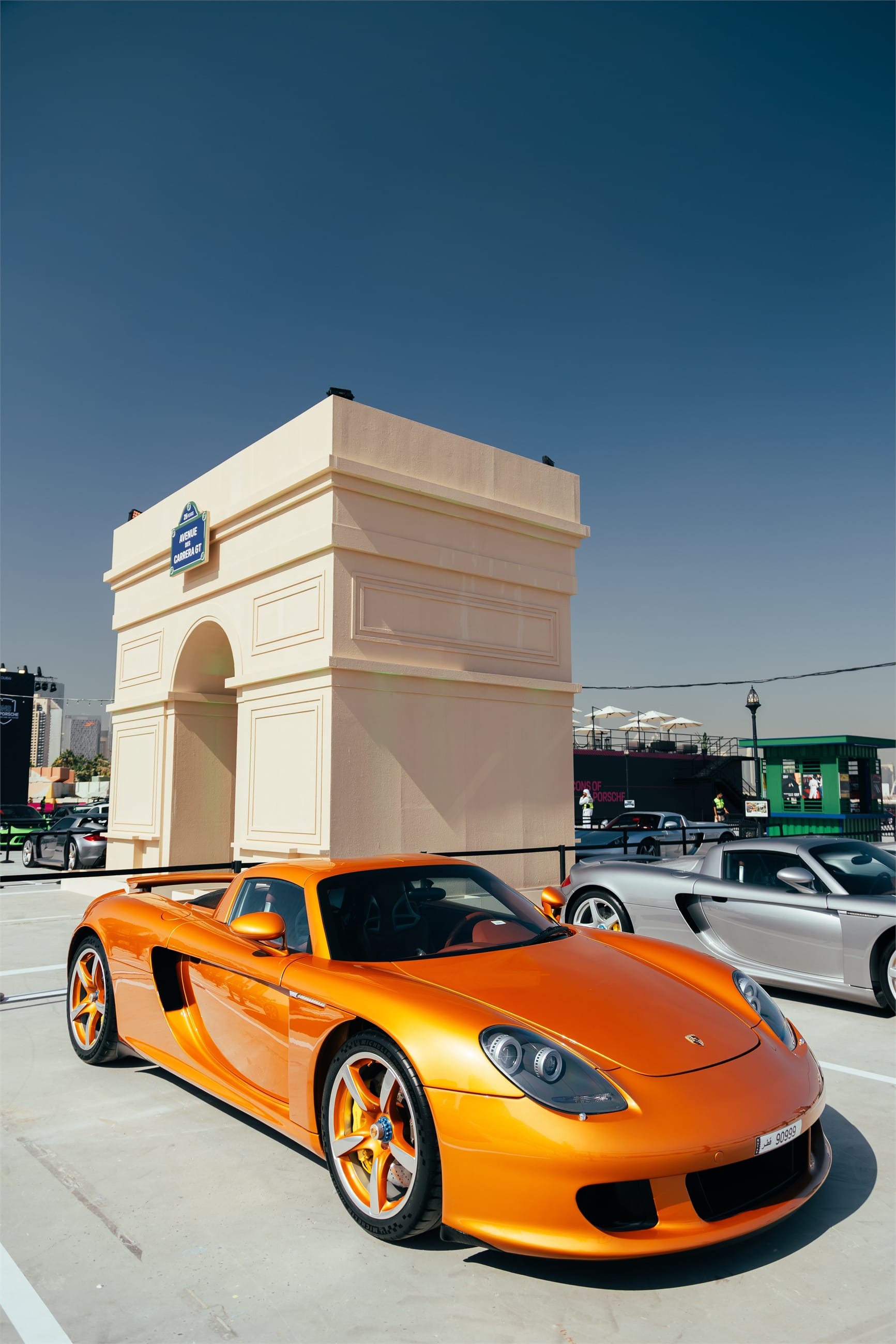 Orange Porsche Carrera GT in front of a miniature triumphal arch.