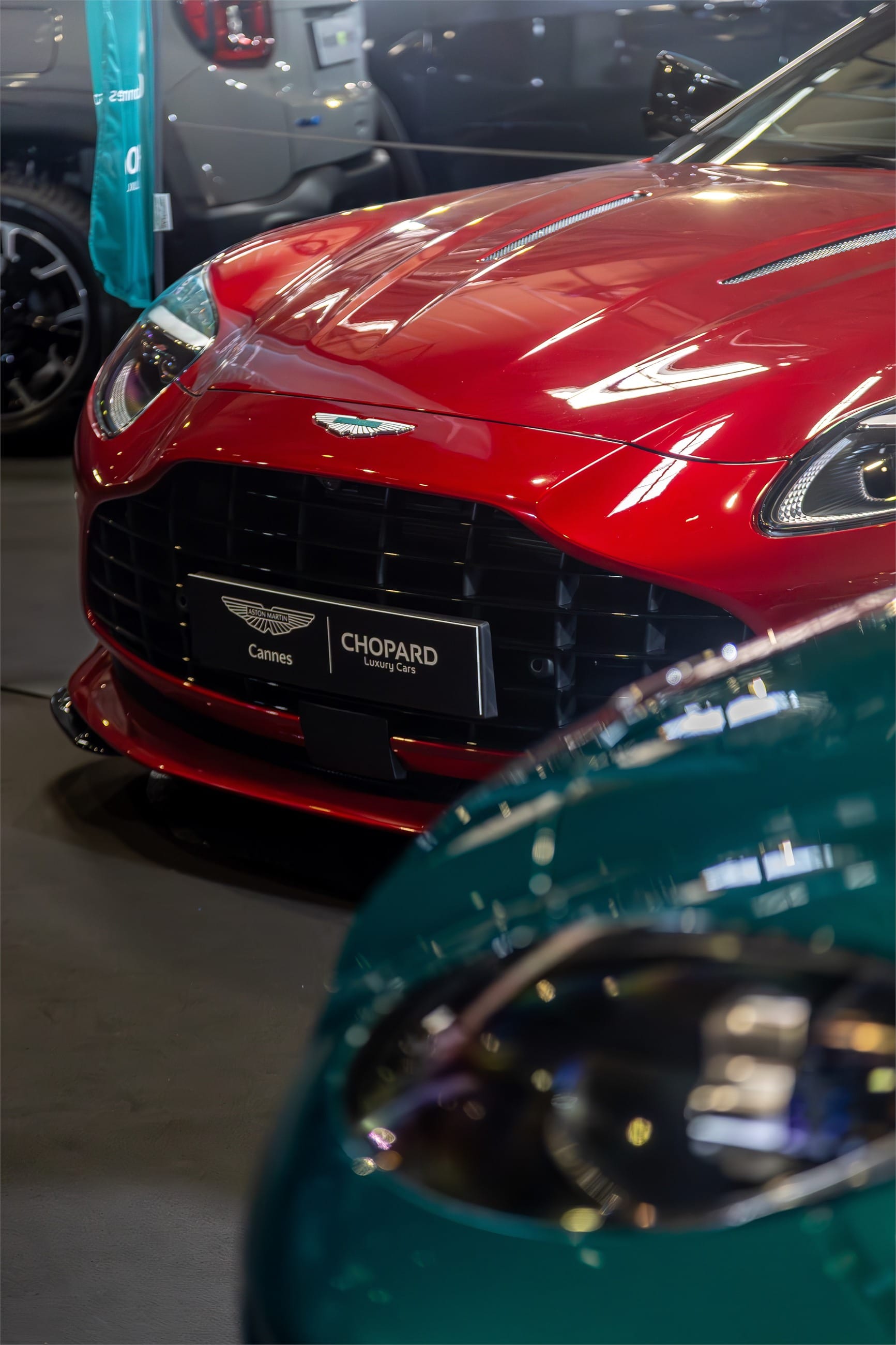 Red Aston Martin coupe beside a green one, seen from above.