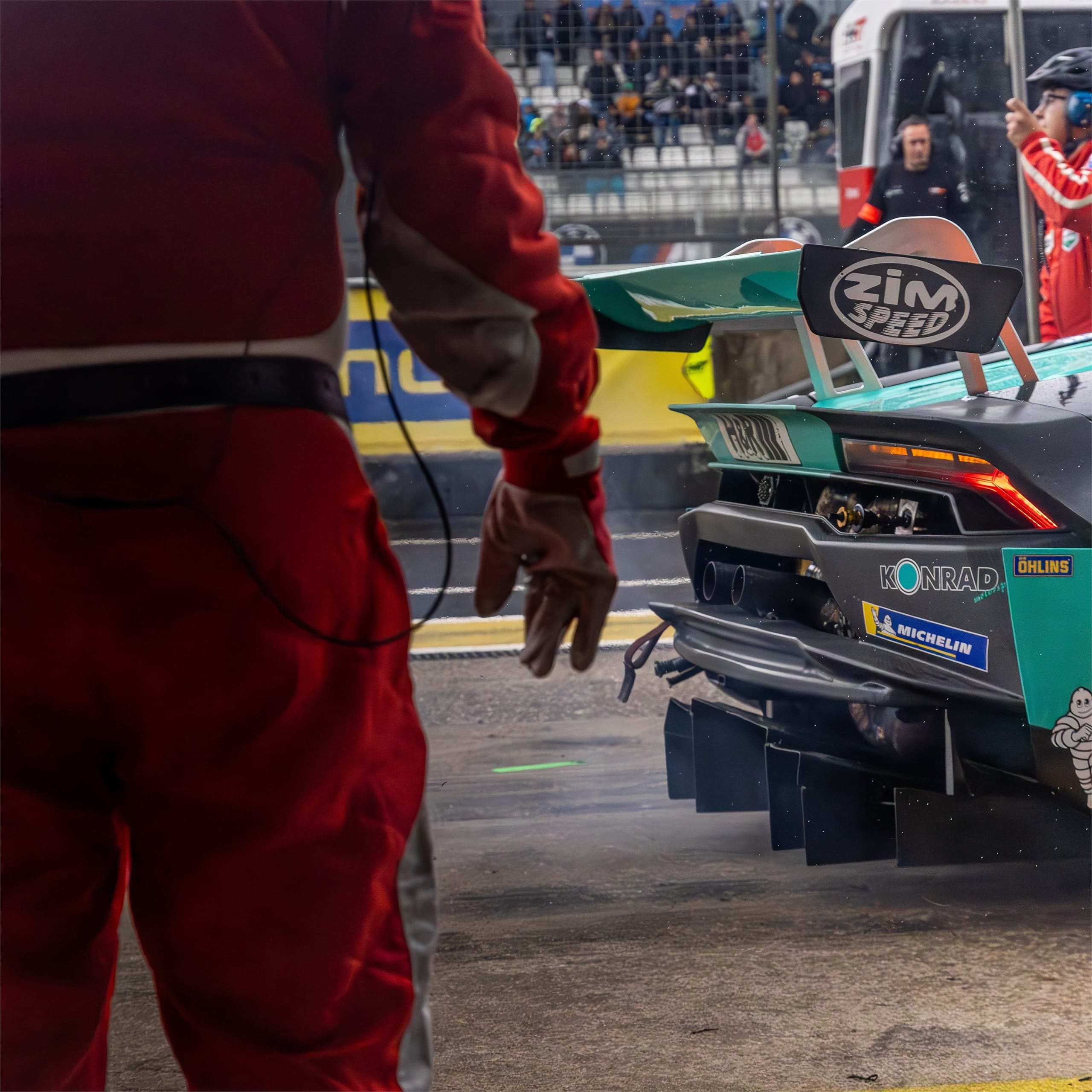 Pit crew in red overalls beside a green racing car in the pit lane.