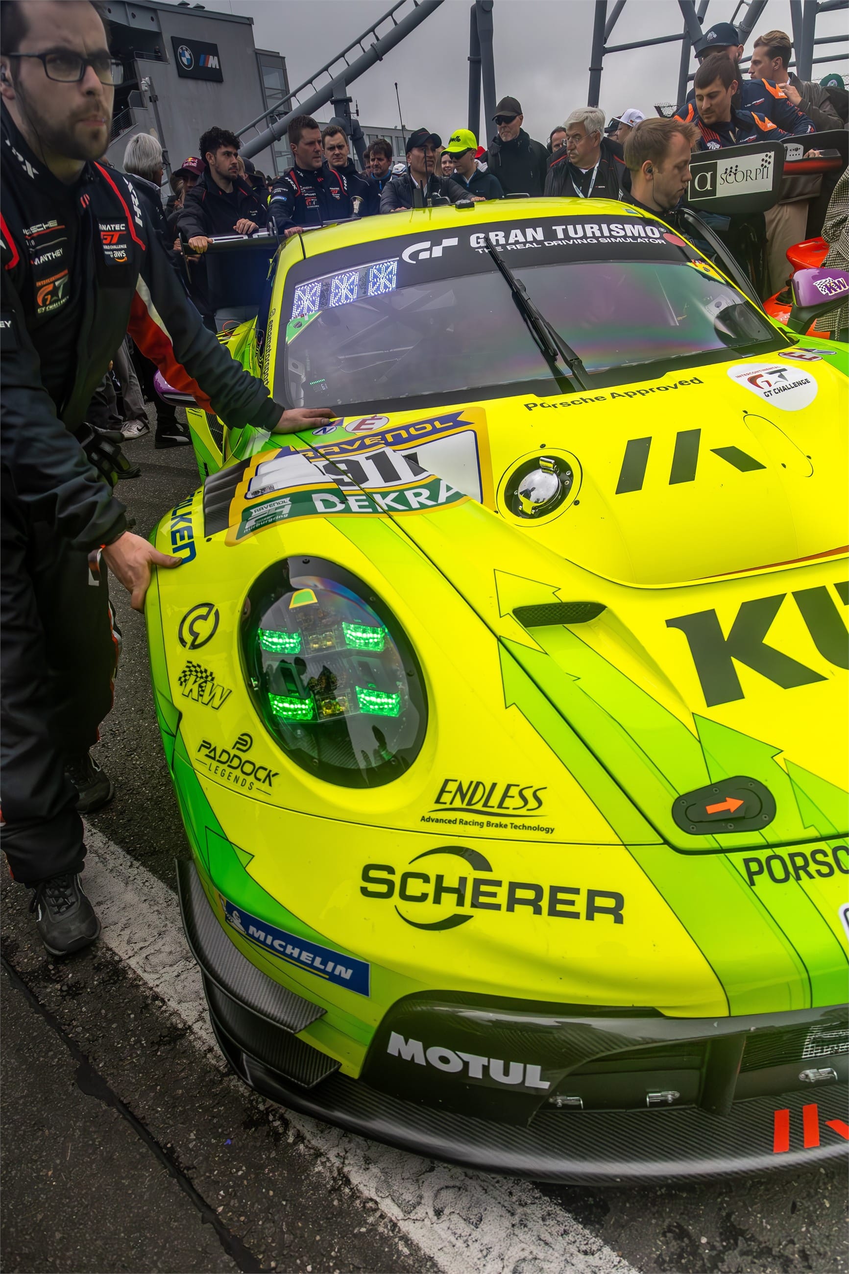 Lime green racing 911 surrounded by its crew on the grid.
