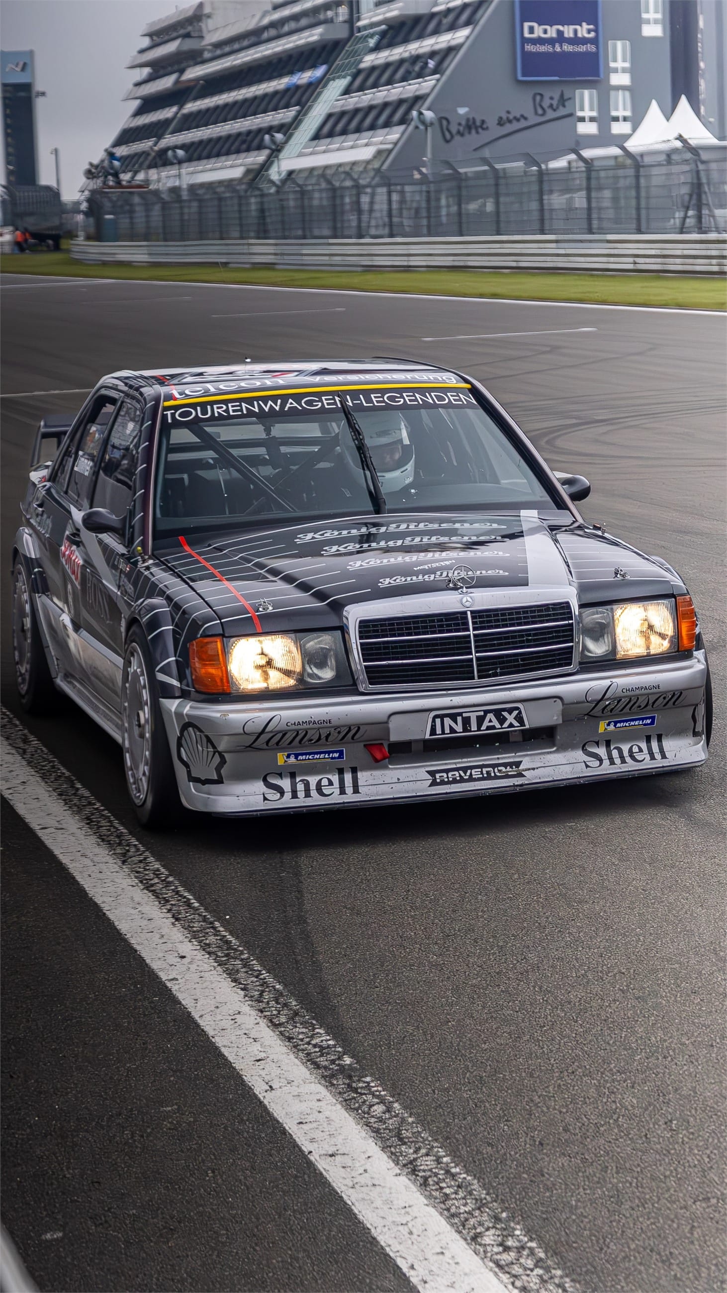 Silver classic touring saloon on the grid, headlights on.