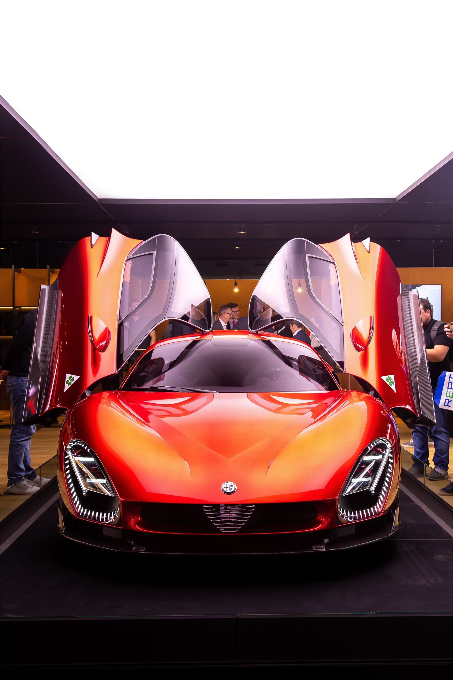 Red and gold coupe with both butterfly doors raised, in a dark showroom.